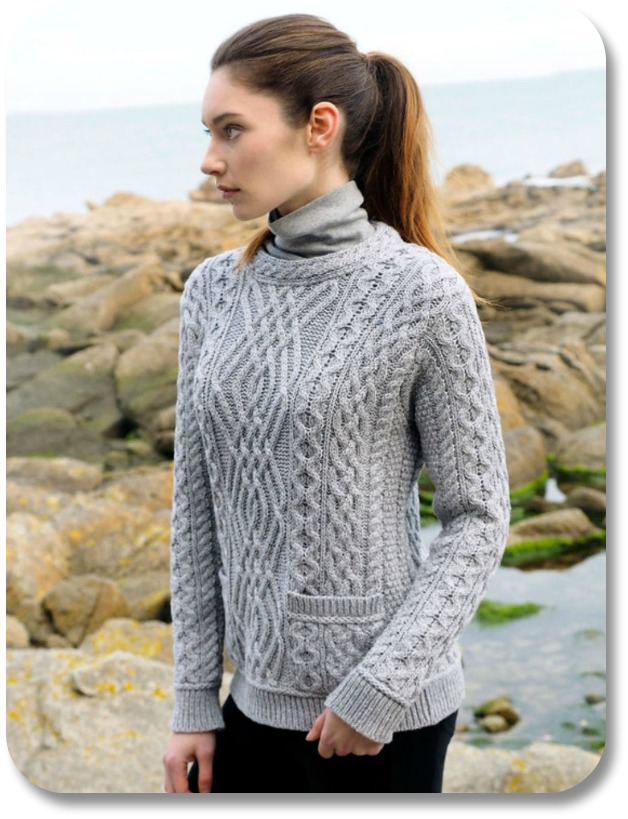 Young woman on stoney beach wearing cable-knit sweater.