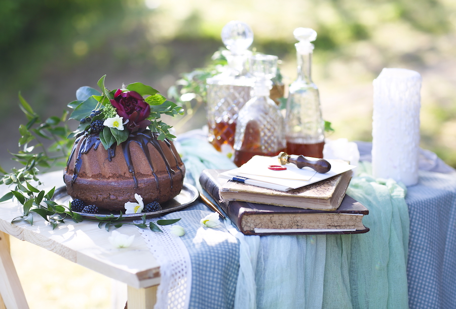 Decorated whiskey cake with cut class containers holding whiskey, white table cloth, blurred background.