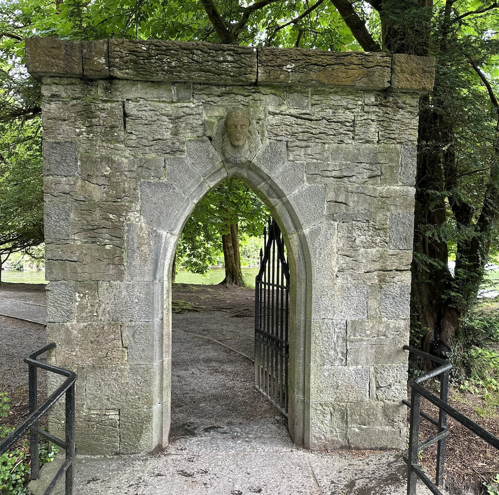 Stone archway with a gate framing a path into the wilderness.