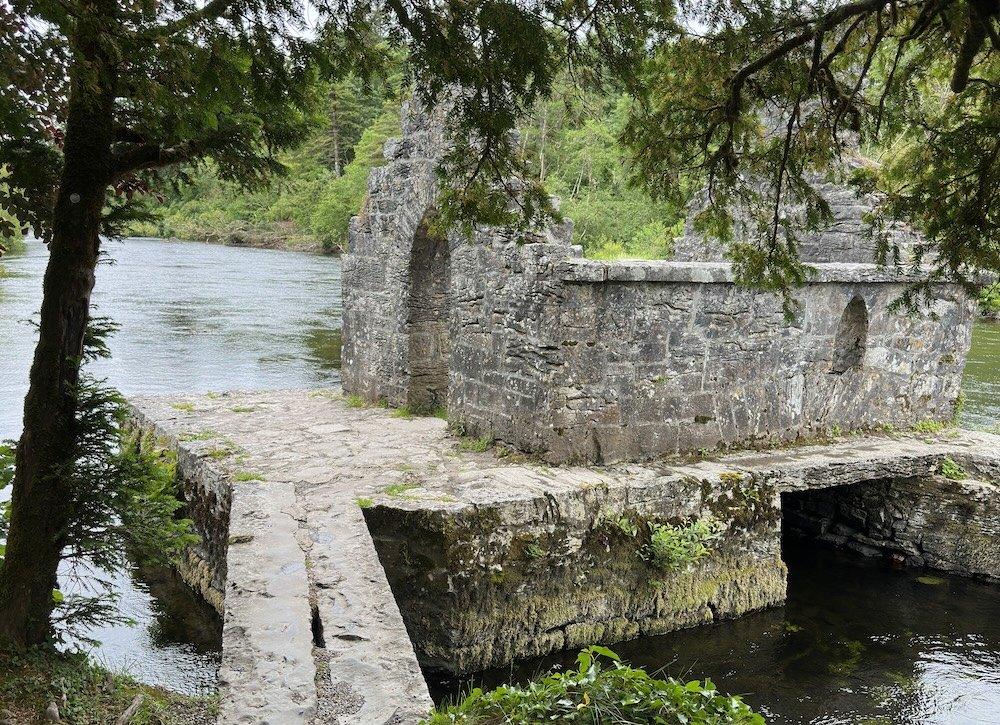 Two wooden planks leading from the shore to a stone structure in the river.