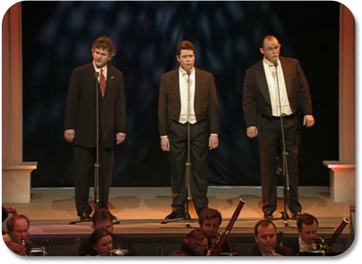 Image of four well-dressed vocalists with microphones singing to an audience.