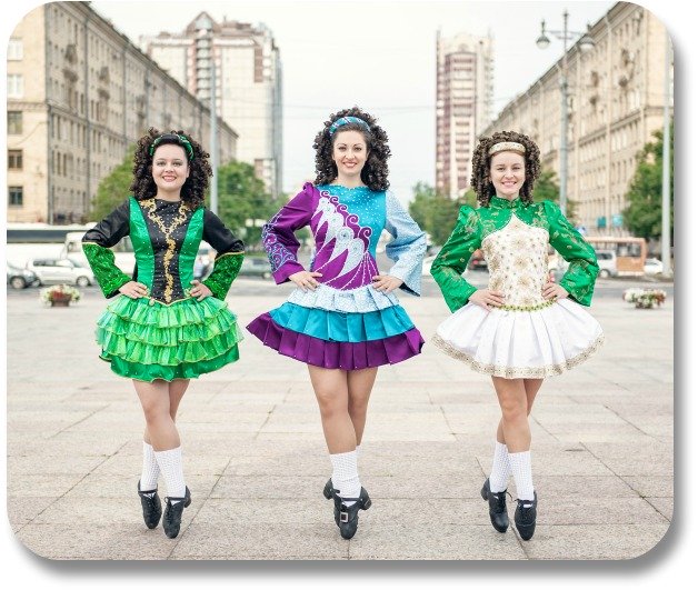 Three young ladies in traditional dance attire performing an Irish jig.