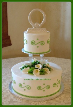 Two layer white wedding cake with green trim and white flowers.